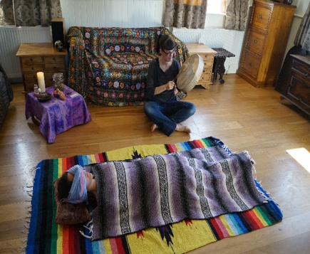 Photo of a woman lying on the floor covered in rebozos while Jo drums.